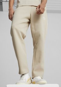 Beige sweatpants med en lös passform och vit Puma-logotyp. Tillverkade av textil med struktur, med sydda detaljer och elastiska muddar.