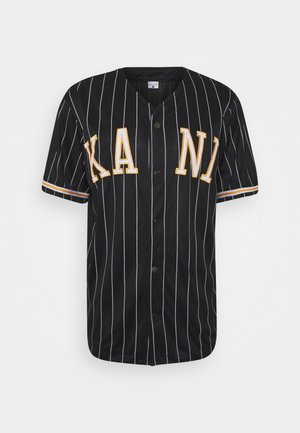 Musta baseball-t-paita valkoisilla pystysuorilla raidoilla, keltaiset "KAN"-kirjaimet, lyhyet hihat, napitettava etuosa ja kontrastiset raidoitetut yksityiskohdat hihoissa.
