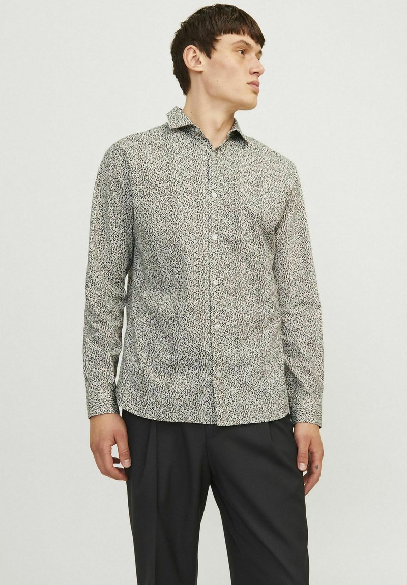 Chemise blanche à manches longues avec un motif abstrait noir et gris, col évasé et coupe ajustée, assortie à un pantalon noir.