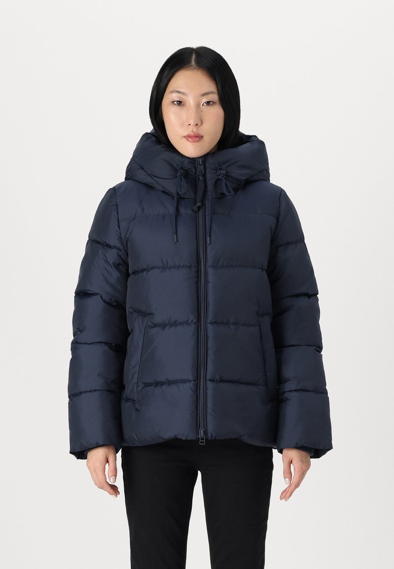 Temno modra puhovka z velikim pokrovom, sprednjim zadrgo in vrvico. Ima prešito zasnovo in elastične manšete.