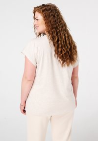 Débardeur léger beige clair à manches courtes en tissu doux, avec un ourlet arrondi et une coupe décontractée, porté avec un pantalon crème.