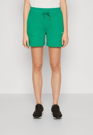 Pantalones cortos deportivos verdes hechos de una tela suave, con una cintura elástica y dobladillos enrollados. Combinados con zapatillas negras.
