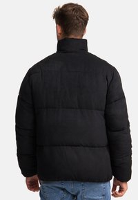Sort puffjakke med høj krave, der har et quiltet design og en glat tekstur. Bagpå ses en løs pasform og sømme.