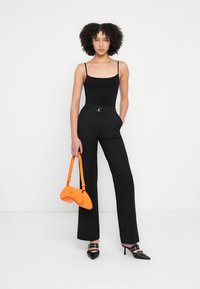 Black spaghetti strap bodysuit, high-waisted black pants with belt, orange handbag, black pointed heels with decorative straps.
