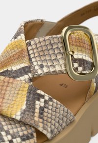 Sandale à talon haut multicolore avec un imprimé python en tons bruns, jaunes et blancs, dotée d'une large boucle et d'une semelle plateforme beige.