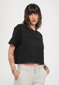 Juodas trumpas t-shirt, pagamintas iš minkštos medvilnės, su trumpomis rankovėmis. Ant krūtinės išsiuvinėtas tekstas "MICHAEL KORS". Lygus paviršius.