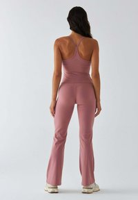 Jasnoróżowy zestaw sportowy składający się z dopasowanego topu na ramiączkach z tyłem typu racerback oraz wysokowstałych, rozszerzanych legginsów wykonanych z gładkiego, elastycznego materiału.