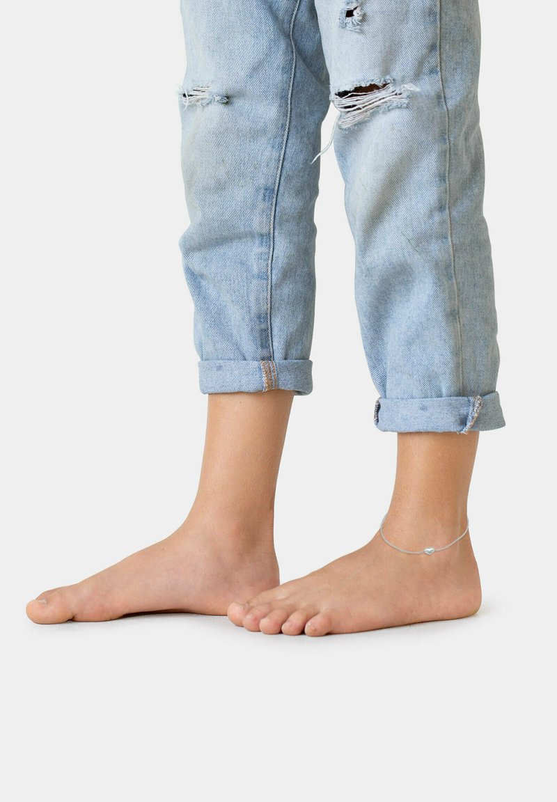 Ljusblå denimjeans med rullade muddar och slitna detaljer, kombinerat med barfota. Ett tunt silverarmband med en hjärtberlock.