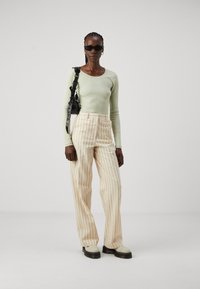 Light green ribbed long-sleeve top, cream striped wide-leg trousers, black handbag, and chunky white platform boots with black soles.