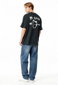 T-shirt en coton noir avec le texte graphique blanc "Mi Amor" et un design de cœur ; associé à un jean bleu clair à coupe relaxée et des baskets blanches.