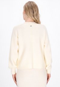 Sweter w kolorze kremowym, wykonany z prążkowanego materiału, o luźnym kroju, z rozcięciem z tyłu i długimi rękawami, teksturowana tkanina i zaokrąglony dekolt.