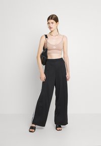 Smeđi skraćeni top s malenim logotipom, uparen s širokim crnim hlačama s bijelim bočnim prugama i debelim crnim sandalama.