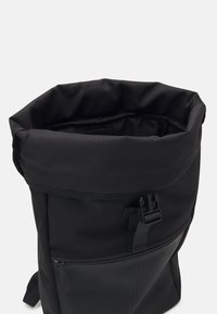 Black roll-top backpack featuring a durable fabric exterior, textured lower panel, front zip pocket, and adjustable side buckles.