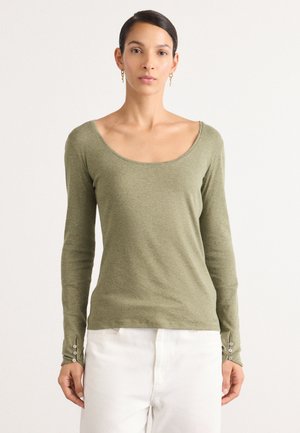 Haut olive à manches longues avec un décolleté arrondi et des accents de boutons sur les manches, associé à un pantalon blanc. Matière douce et légère.