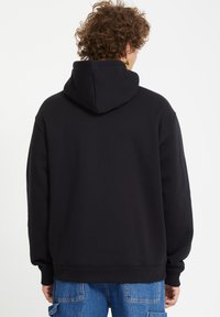 Zwarte hoodie met een zachte textuur, losse pasvorm, geribde boorden en zoom. Heeft een verstelbare capuchon en geen zichtbare graphics.