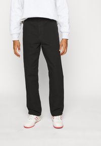 Schwarze Baumwollmischungshose mit geradem Bein, versehen mit Fronttaschen und einer glatten Textur, kombiniert mit weißen Turnschuhen.