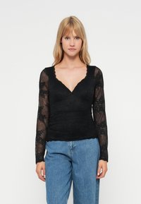 Zwarte lange mouwen top met kantstructuur, V-hals ontwerp en geplooide stof bij de taille, gecombineerd met hoge taille blauwe jeans.