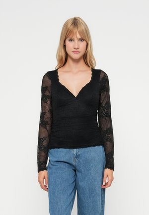 Czarny długi rękaw top z koronkową fakturą, zaprojektowany w dekolcie w kształcie litery V, z marszczonym materiałem w talii, połączony z niebieskimi dżinsami o wysokim stanie.