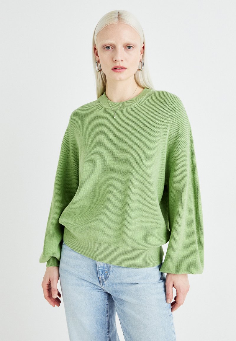 Grønn strikket genser med en avslappet passform, ribbestruktur, rund hals og dropped skuldre. Kombinert med lyse vasket jeans.