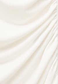 Tissu blanc doux avec un détail de fronces rassemblées le long du côté droit créant des plis texturés et des ombres.