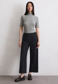 Harmaa lyhythihainen mock neck -paita yhdistettynä mustiin leveälahkeisiin housuihin ja ruskeisiin loafer-kenkiin. Sileä kangas, hyvin istuva ja siistit linjat.