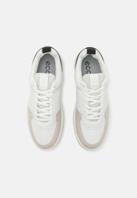 Balti odiniai sportbačiai su perforuotu dizainu, smėlio spalvos akcentais priekyje, pilka tekstilės pašiltinimu ir juoda kulno juosta.