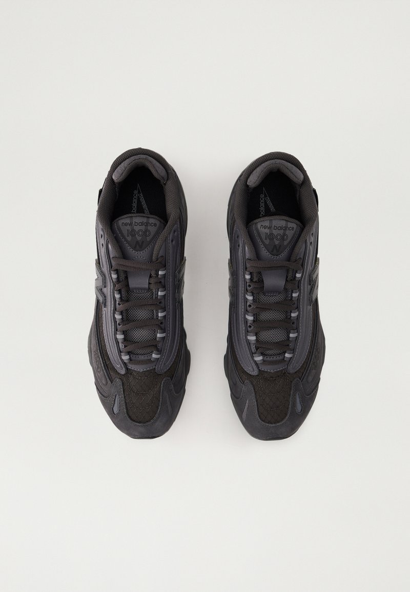 Des chaussures de sport noires présentant une combinaison de surfaces lisses et texturées, un design à lacets, et de subtils accents gris sur les côtés.