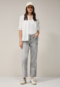 Lichtgrijze broek met voorzakken, gecombineerd met een wit tanktop en een wit overhemd met knopen. Witte sneakers maken de outfit compleet.