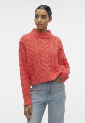 Maglione a coste corallo con collo alto, orlo spesso a coste e maniche oversized, abbinato a jeans azzurri chiari.