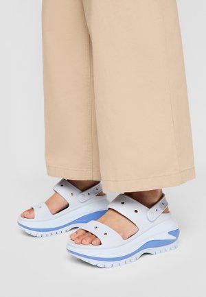 Stopy w białych i niebieskich sandałach na platformie z regulowanymi paskami, zestawione z beżowymi spodniami o szerokich nogawkach.