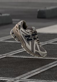 Beige sportskor med övre mesh, svarta detaljer, vadderad krage och en dämpad sula, designad för komfort och stöd under aktiviteter.