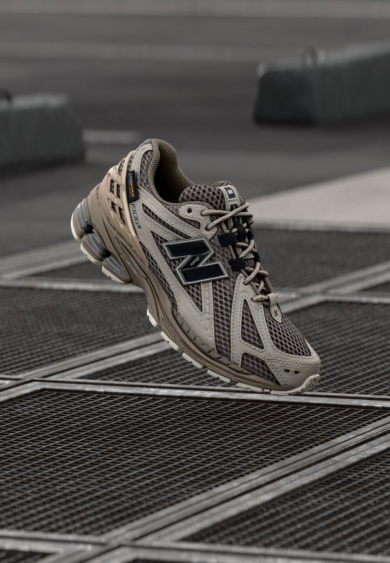 Beige athletic shoe with mesh upper, black accents, padded collar, and a cushioned sole, designed for comfort and support during activities.