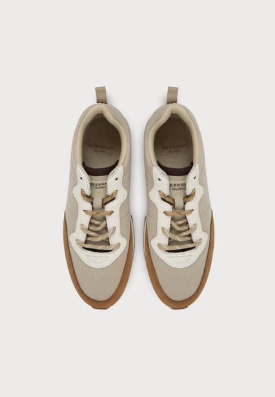 Ζευγάρι μπεζ και λευκά casual sneakers με καφέ λεπτομέρειες και κορδόνια, σε θέα από ψηλά σε απλό φόντο.