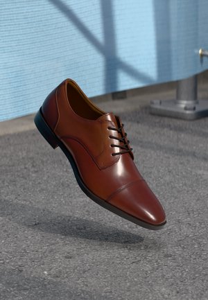 Braune Lederdressschuhe mit glatter Oberfläche, Schnürdesign, spitzer Zehenform und dezenten Stickdetails. Schwarze Gummisohle.