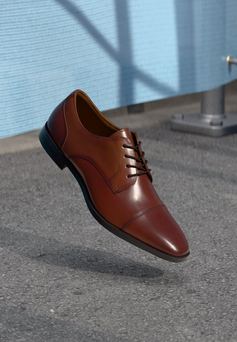 Chaussure habillée en cuir brun avec une finition lisse, un design à lacets, un bout pointu et des détails de couture subtils. Semelle en caoutchouc noir.