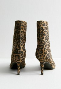 Botines de tela con estampado de leopardo, que presentan una puntera afilada y un tacón delgado. El patrón es una mezcla de marrón y negro.