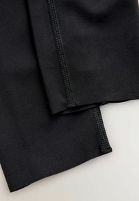 Fekete sport-legging, sima felülettel, lapos derékpánttal és megerősített varrással a varratok mentén a tartósság és a kényelem érdekében.