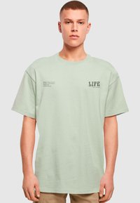 Lys grøn bomuld T-shirt med korte ærmer, rund halsudskæring og trykte tekster med "LIFE" og citater på forsiden og siden.