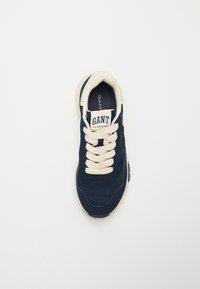 Adidași bleumarin cu un superior din suede și plasă, șireturi crema și o talpă din cauciuc. Dispune de un logo pe limbă și pe panoul lateral.