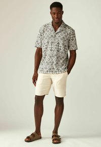 Camisa de manga corta con un patrón geométrico en blanco y negro, combinada con pantalones cortos beige y sandalias marrones, con un diseño de botones.