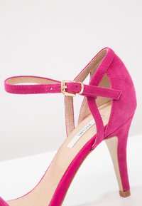 Sandale à talon haut en daim fuchsia avec bride de cheville, détail de boucle dorée, design à bout ouvert et talon stiletto. Doublure intérieure lisse.