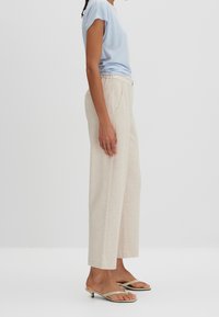 Top corto de color azul claro de manga corta combinado con pantalones anchos color crema. El atuendo incluye sandalias de tacón beige, enfatizando un estilo relajado y casual.