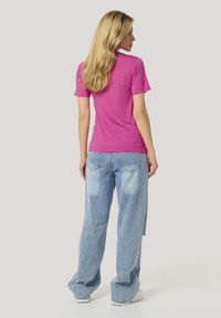 T-shirt rose ajustée à manches courtes, associée à un jean en denim léger bleu clair. Le tissu semble lisse et léger.