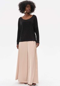 Schwarzes Langarmoberteil mit dezenten Verzierungen, kombiniert mit weiten beigen Hosen, die eine glatte Textur und einen lockeren Schnitt aufweisen.