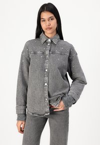 Veste en denim gris avec boutons pression, manches longues et embellissements en cristal à l'avant. Elle présente un col classique et une coupe décontractée.