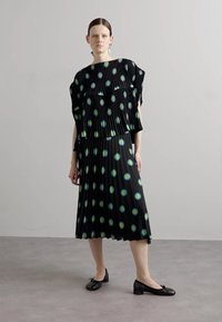 Black pleated dress with turquoise and green circular patterns, paired with black flats. Features a loose-fitting top and long skirt.