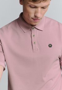 Korte mouw polo shirt in lichtroze, gemaakt van gestructureerde stof, met een kraag, drie knopen en een hexagonaal logo op de borst.