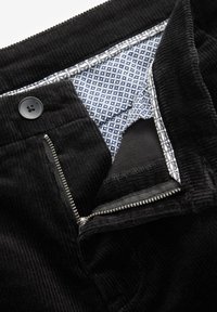 Pantaloni in velluto nero con chiusura a zip e bottone. L'interno presenta una fodera a fantasia blu navy con accenti bianchi, realizzata in un tessuto morbido.