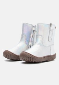 Iridescente hvite ankelstøvler med en sprukket tekstur, brun gummisåle og glidelås på siden. Har en pull tab bak.