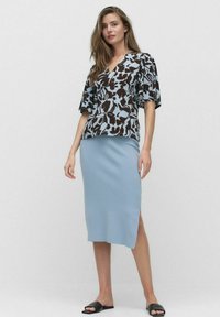 Bloempatronen blouse in lichtblauw en bruin, gecombineerd met een aansluitende lichtblauwe gebreide midi-rokken. Gemaakt met zwarte slide sandalen.